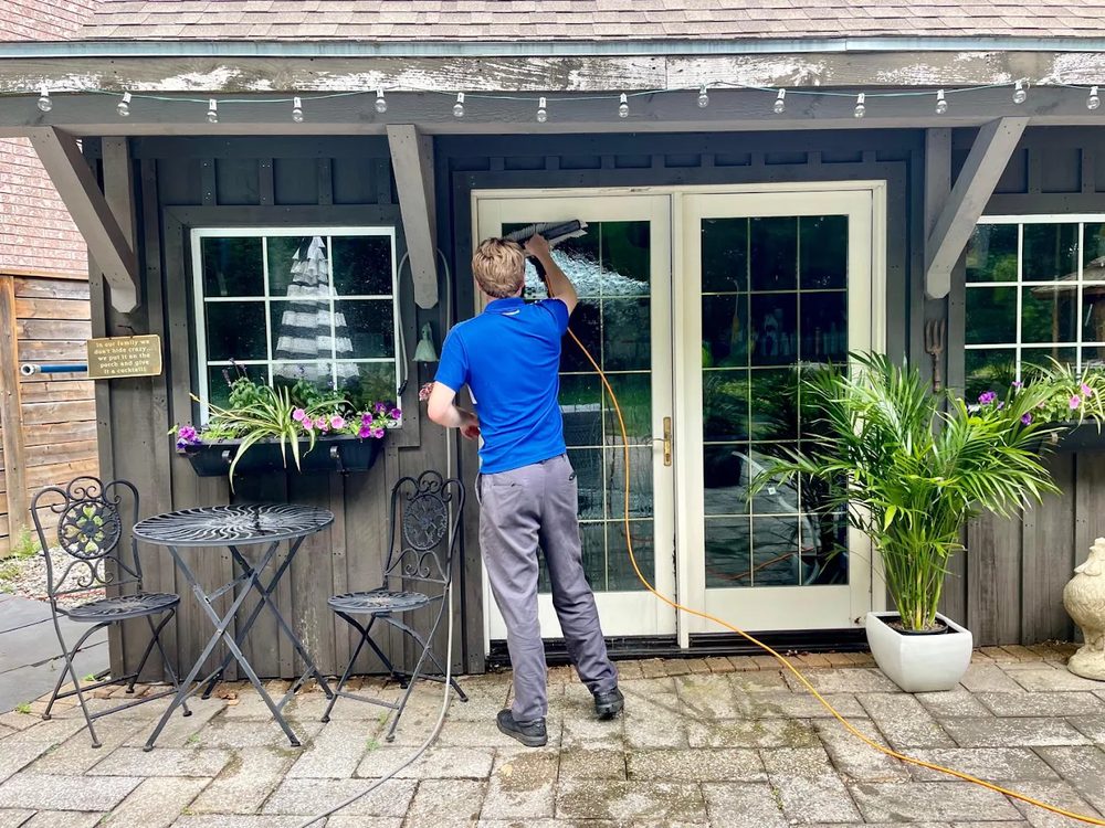 Window cleaner scrubbing the glass of French doors on a home patio