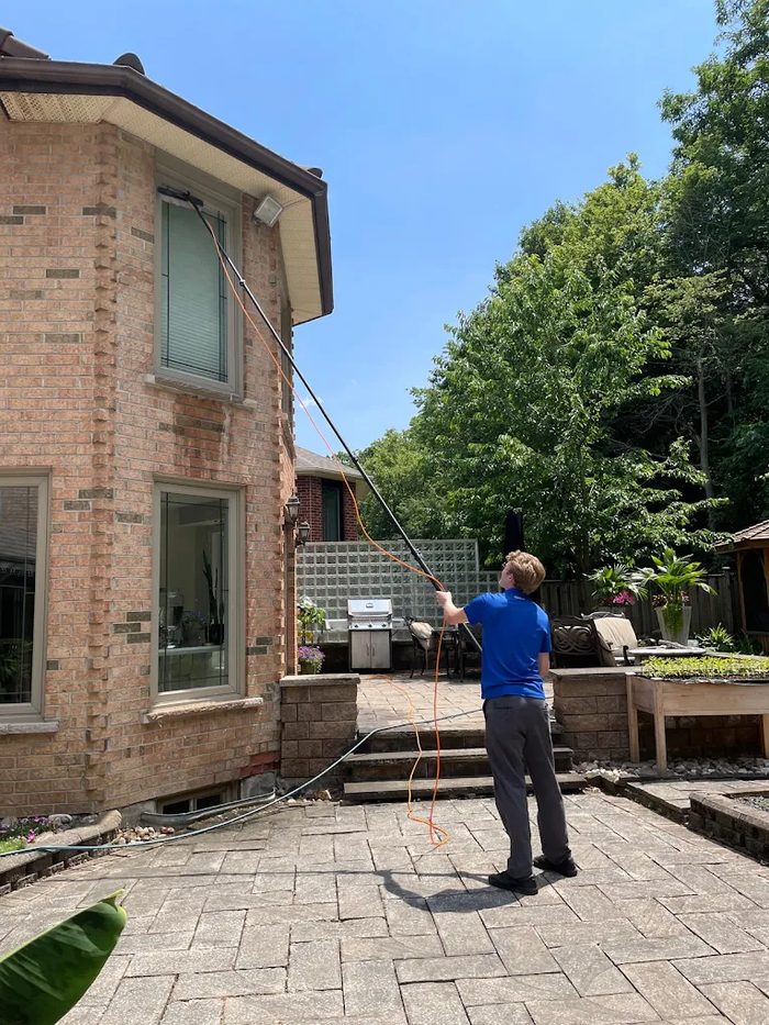 Window cleaner using a long pole to clean the upper windows of a brick house